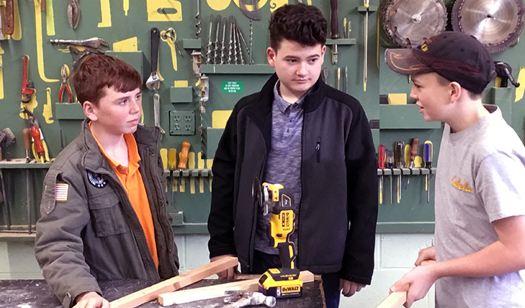 Three boys talking over their wood working project.
